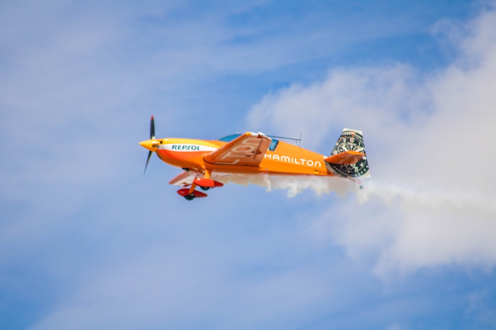 a small orange airplane flying through a blue sky