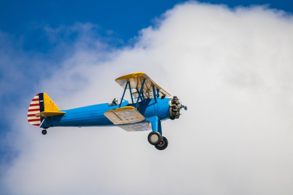 a small blue airplane flying through a cloudy blue sky