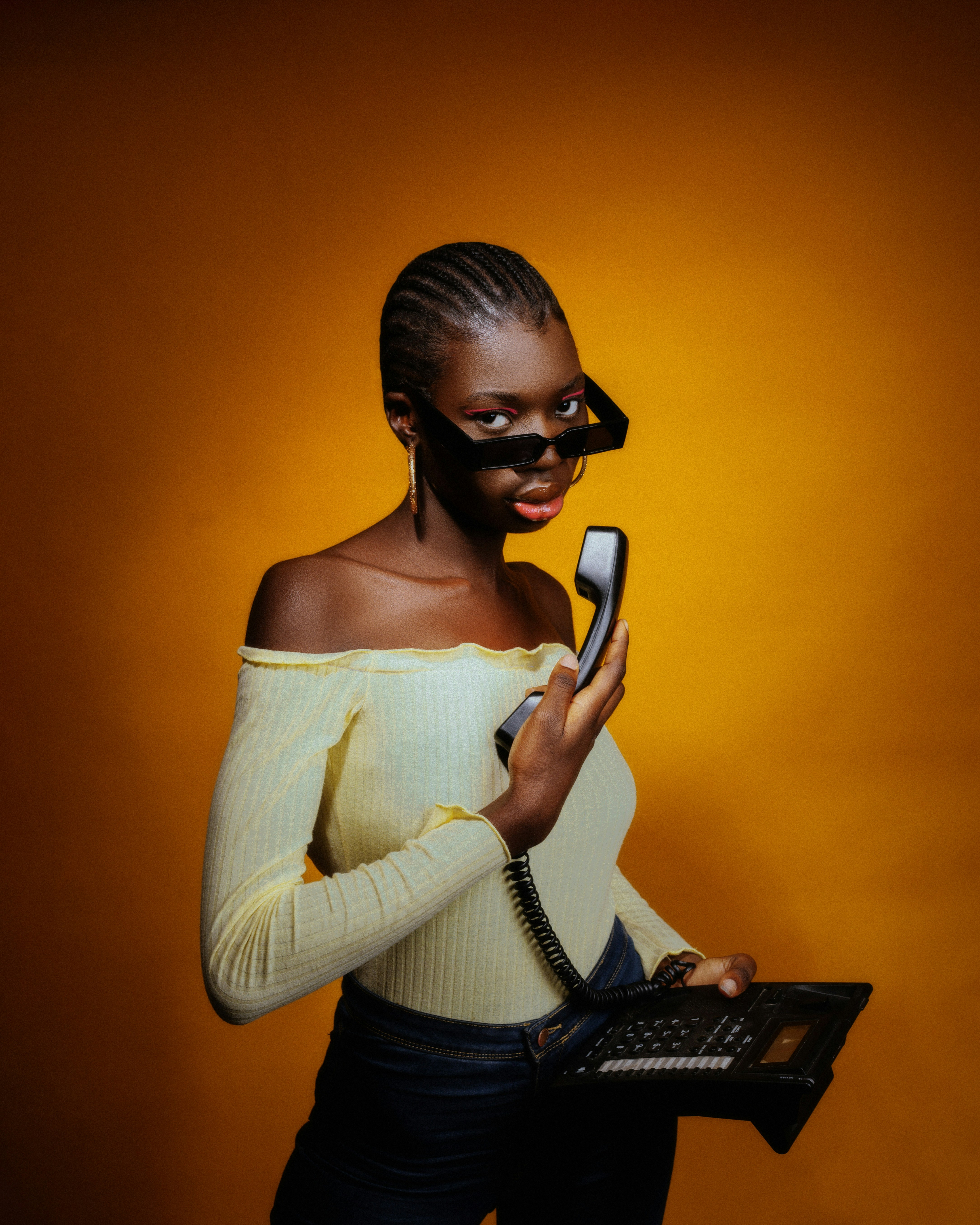 Stylish woman with sunglasses holding a vintage telephone receiver.