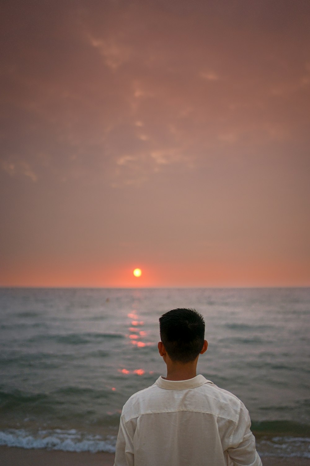 um homem sentado em uma praia observando o pôr do sol