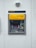 A modern ATM embedded in a wall, featuring a bright yellow panel with the word 'geldmaat' on it. The machine includes a screen displaying text, a numeric keypad, and card slots. Above the ATM, there's a sign with the text 'opnemen'. The background is a light gray wall with a small, round light fixture on top.