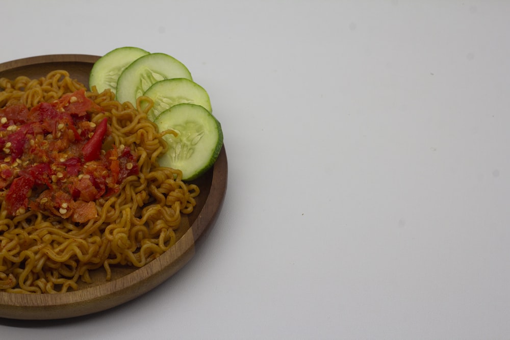 a wooden bowl filled with noodles and cucumbers