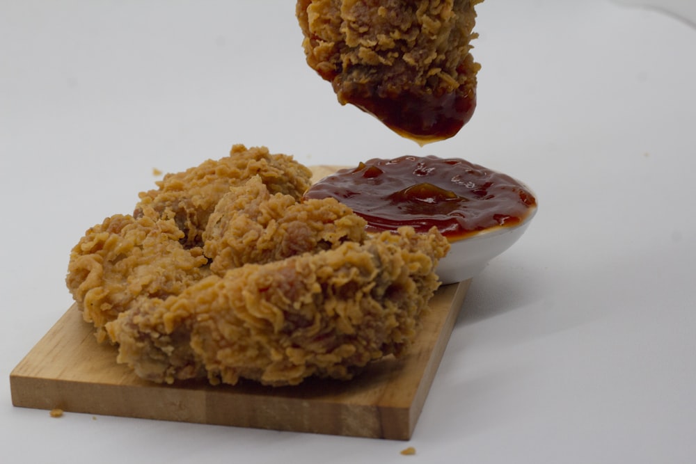 a wooden board topped with fried food next to a bowl of ketchup