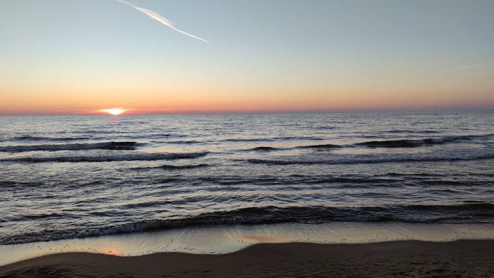 the sun is setting over the ocean on the beach