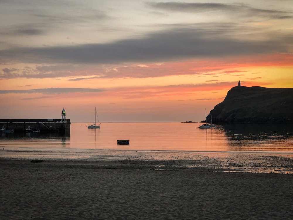 a beach with boats in the water at sunset