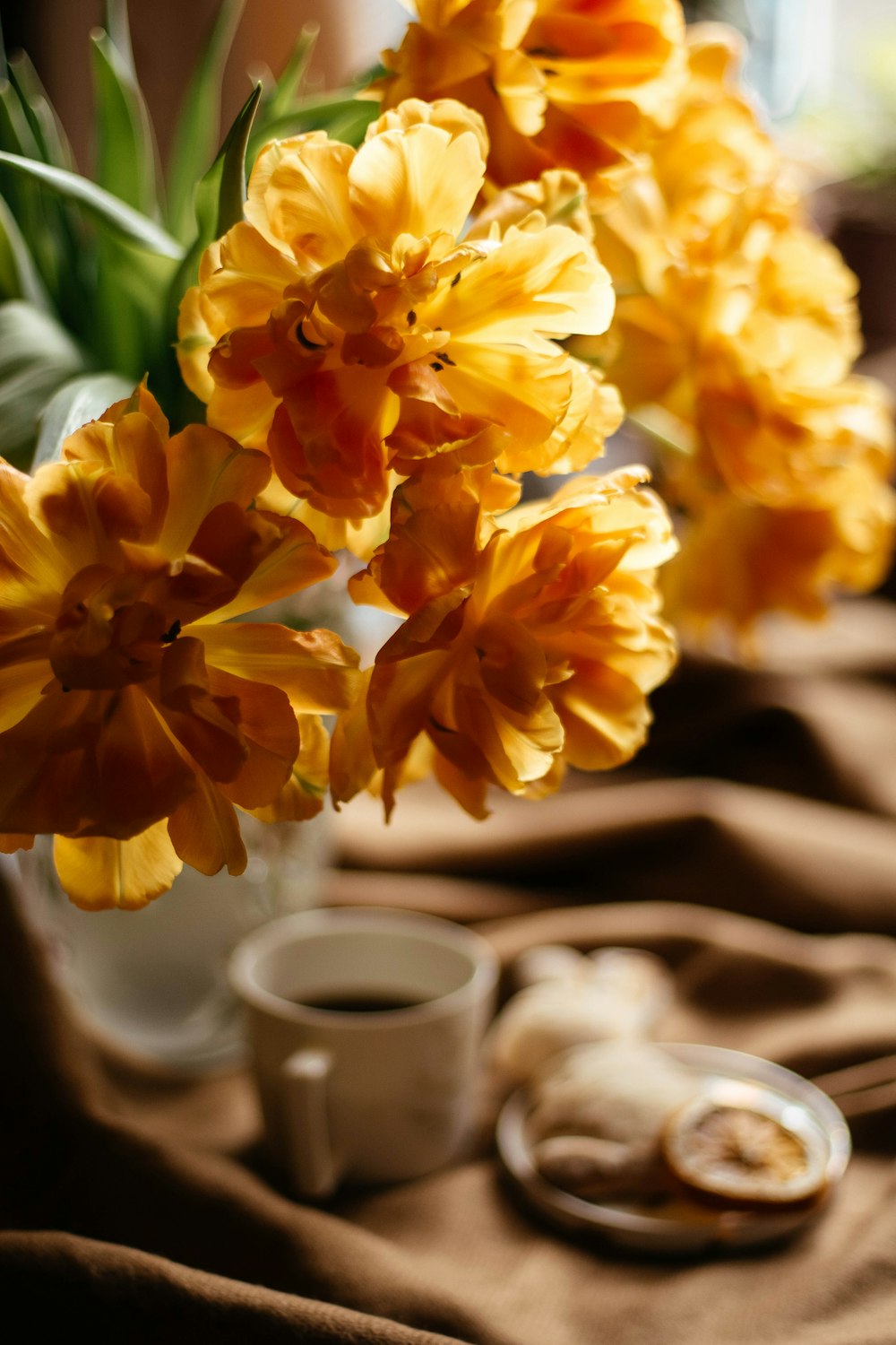 a vase filled with yellow flowers next to a cup of coffee