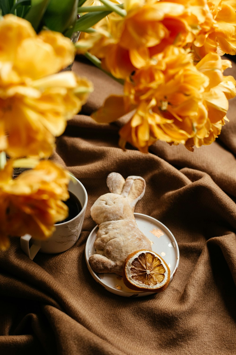 a stuffed rabbit sitting on a plate next to some flowers