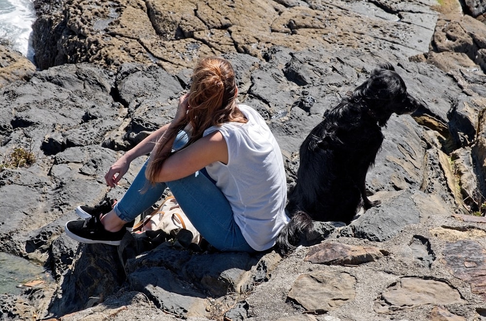 a woman sitting on a rock next to a black dog