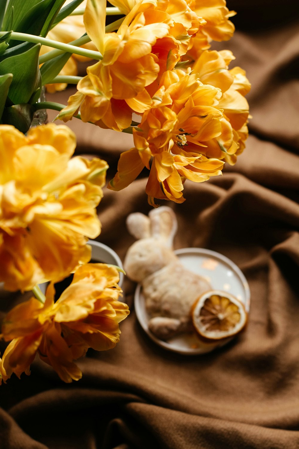yellow flowers and a plate of food on a brown cloth