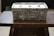 A rectangular stone-textured container filled with white material, possibly wax, positioned on a dark wooden table. Three wooden wicks are visible emerging from the wax-like substance.