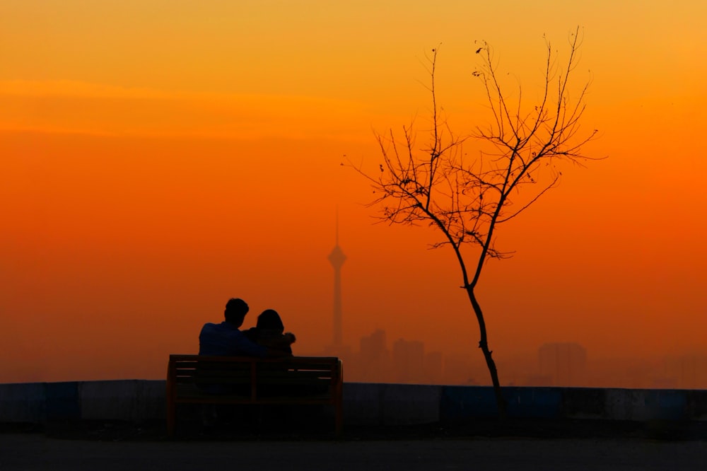 two people sitting on a bench at sunset