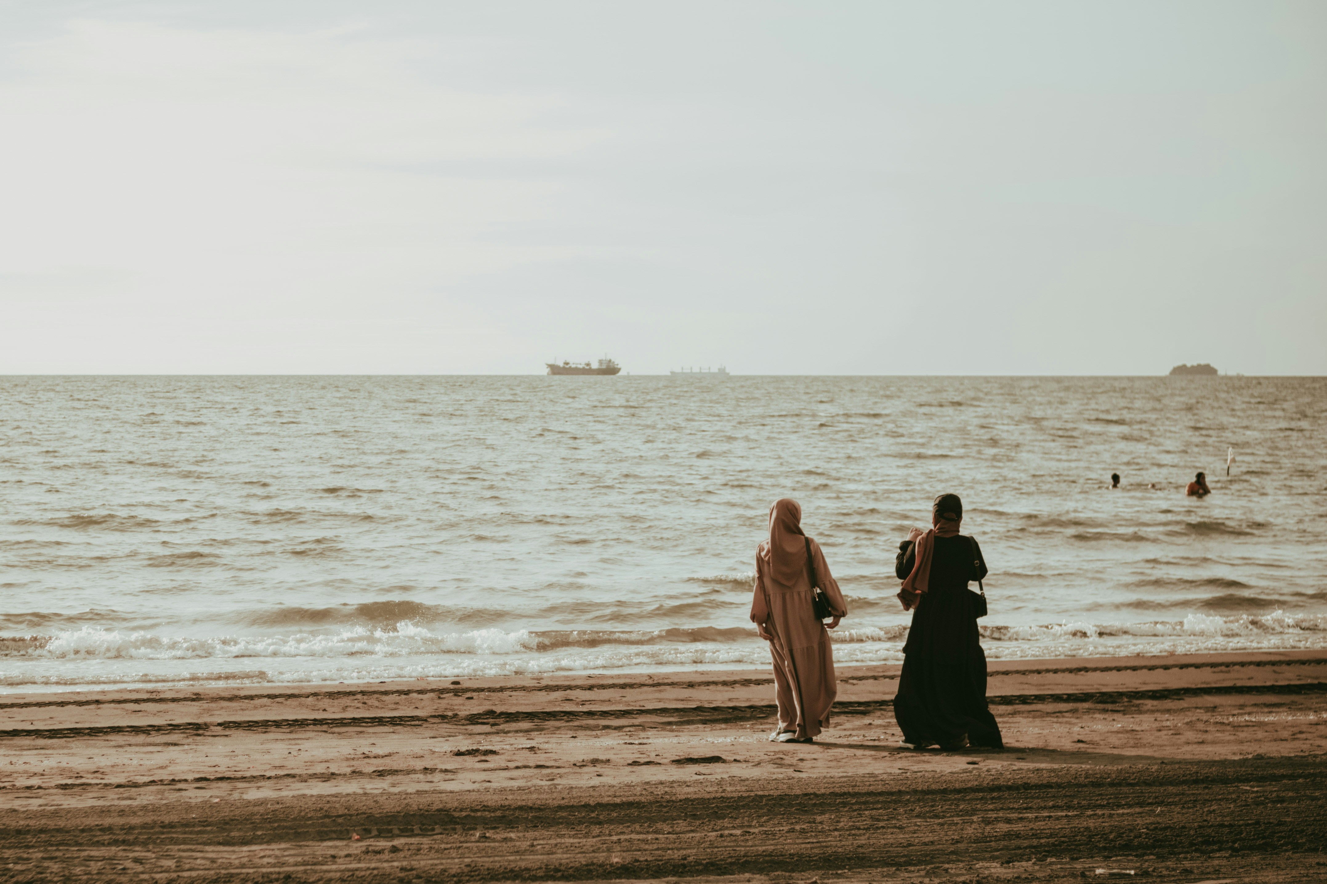 a couple of women standing on top of a sandy beach