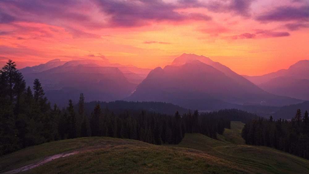 a sunset view of a mountain range with trees in the foreground