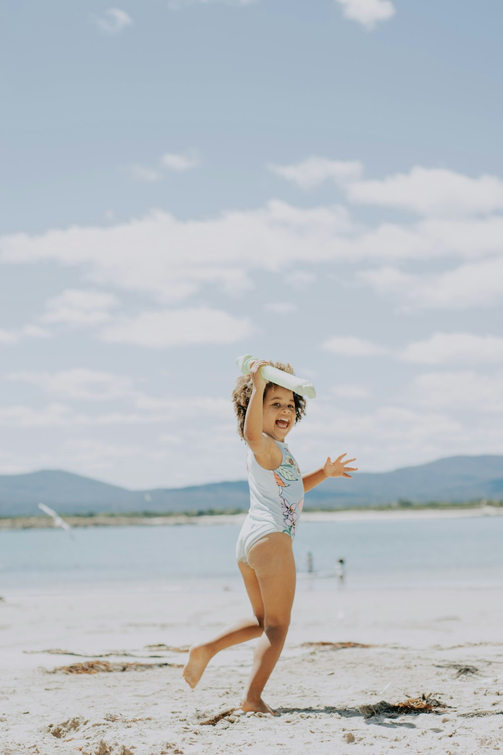 a little girl running on the beach with a hat on