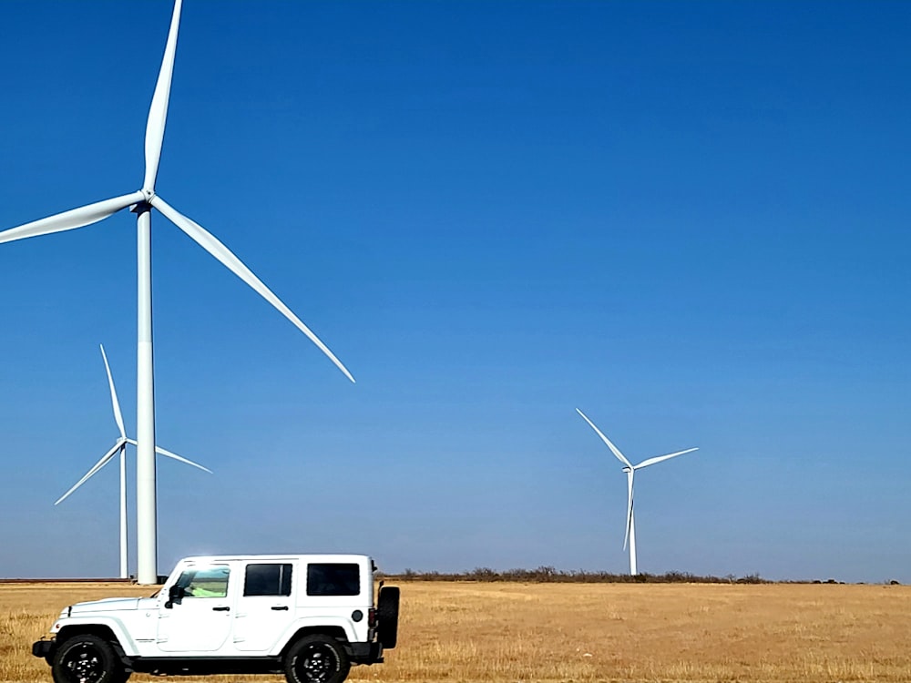 a white jeep parked in front of a wind turbine