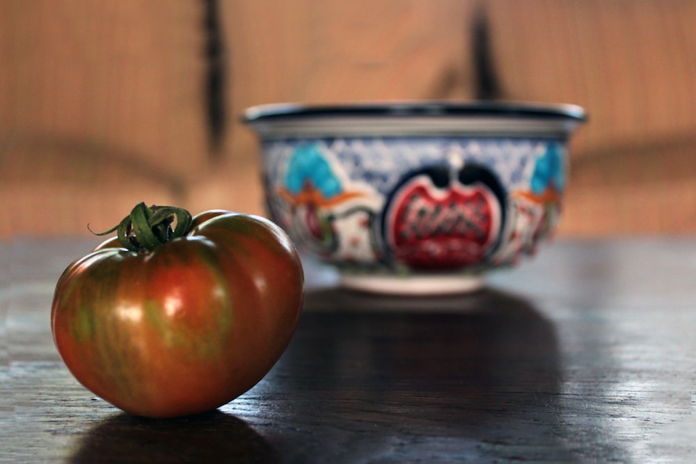 a tomato sitting next to a bowl on a table