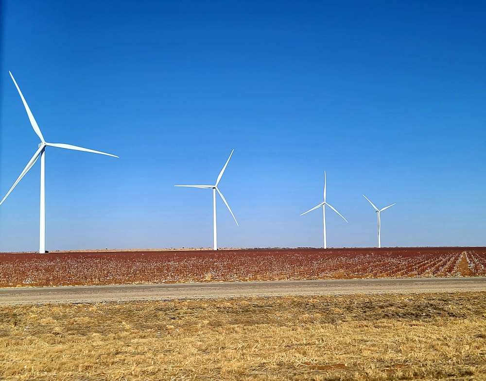 three wind turbines in a field with a dirt road in the foreground