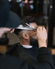 A barber carefully shaping a client's haircut with scissors and comb in a cozy barbershop setting.