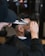 A barber is using scissors and a comb to trim the hair of a seated client with a beard. The setting appears to be a barbershop with a blurred background indicating other salon equipment or decor.