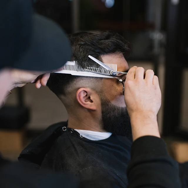 A barber cutting another man's hair with a pair of scissors in a barbershop