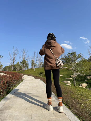 Model wearing a pastel terracotta hoodie walking through a sunlit urban park.