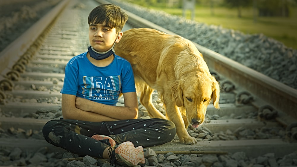 a young boy sitting on a train track with his dog