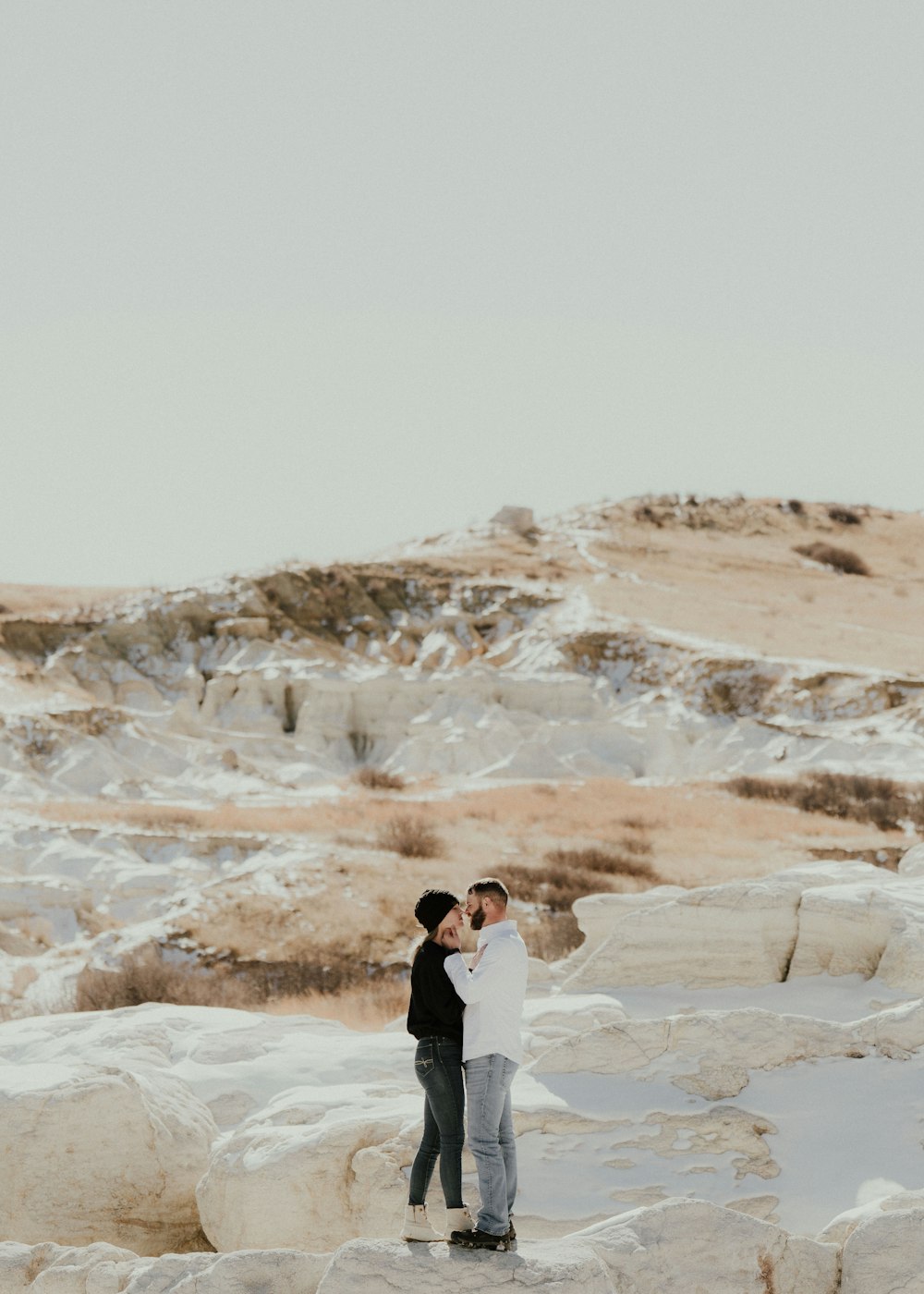 a man and a woman standing on a rock in the snow