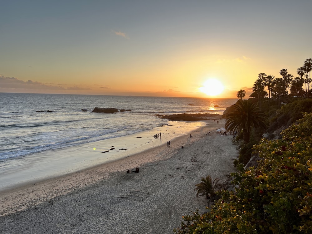 the sun is setting over the beach with people on it