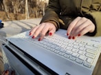 a woman with red nails typing on a white keyboard