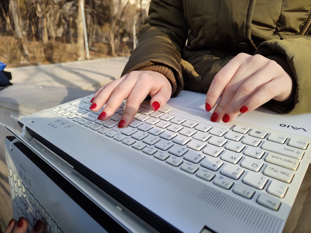 a woman with red nails typing on a white keyboard