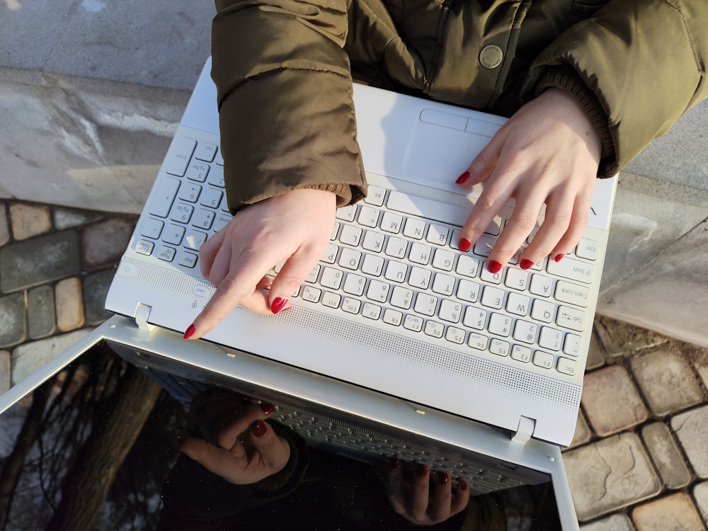 Una mujer está escribiendo en una computadora portátil blanca