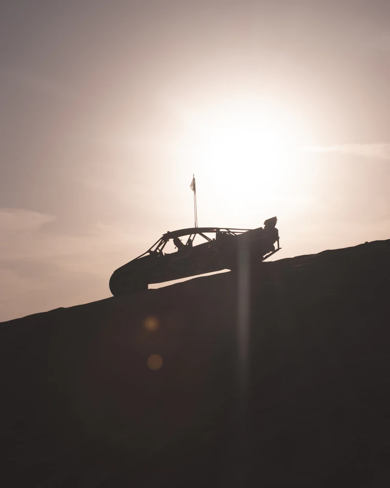 Off-road buggy silhouetted on a hillside against the sun