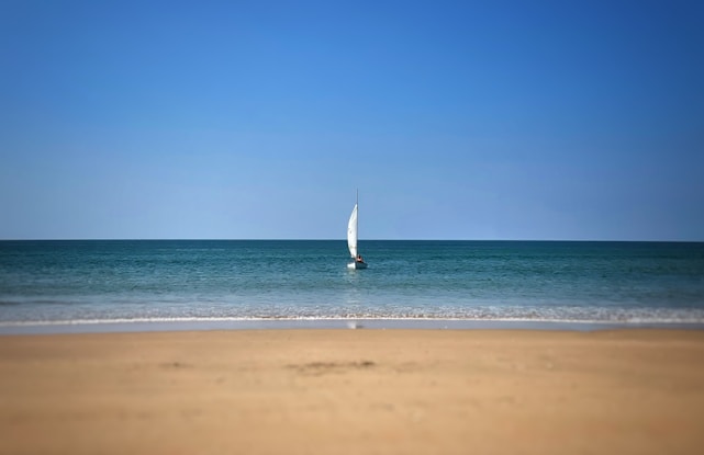 A sailing instructor guiding a student on a small boat with bright blue sky and calm sea in the background