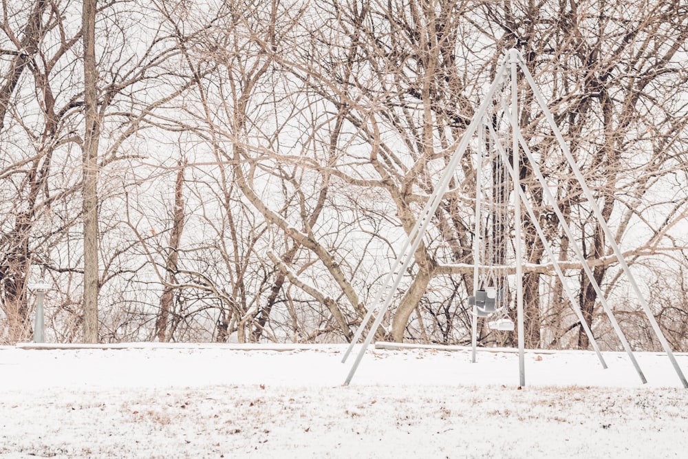 a swing set in the snow with trees in the background