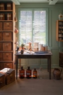 A serene, sunlit room with natural wood accents and a small collection of Genesis Apothecary bottles arranged beside a potted plant.