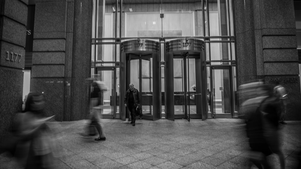 a black and white photo of people walking in front of a building