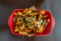Golden crispy fries served in a red container with a side of spicy dipping sauce.