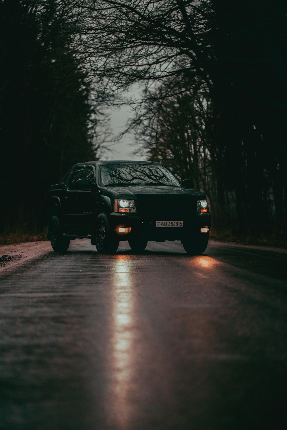 a black truck driving down a wet road