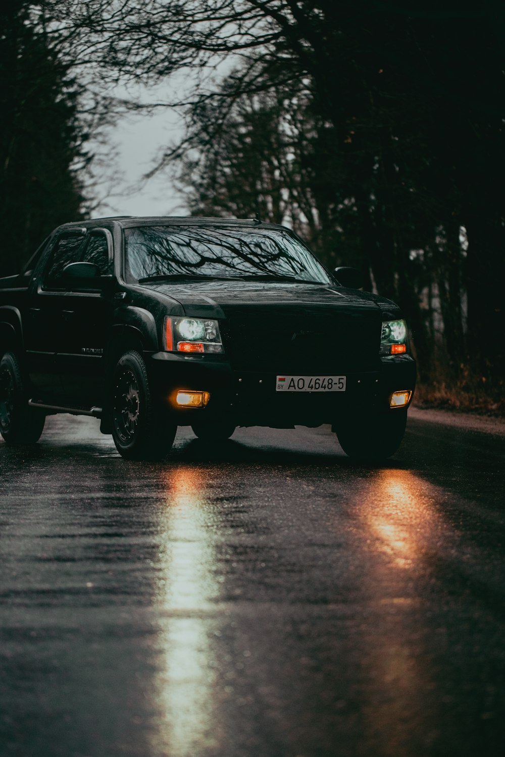 a black truck driving down a rain soaked road