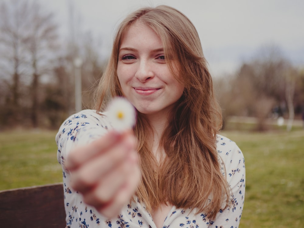 a woman pointing at the camera with a flower in her hand