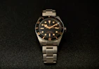 a watch sitting on a black surface with gold numbers