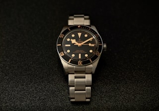 a watch sitting on a black surface with gold numbers