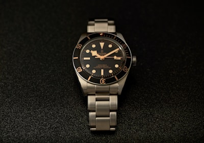 a watch sitting on a black surface with gold numbers