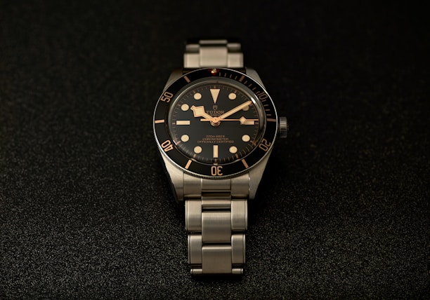 a watch sitting on a black surface with gold numbers