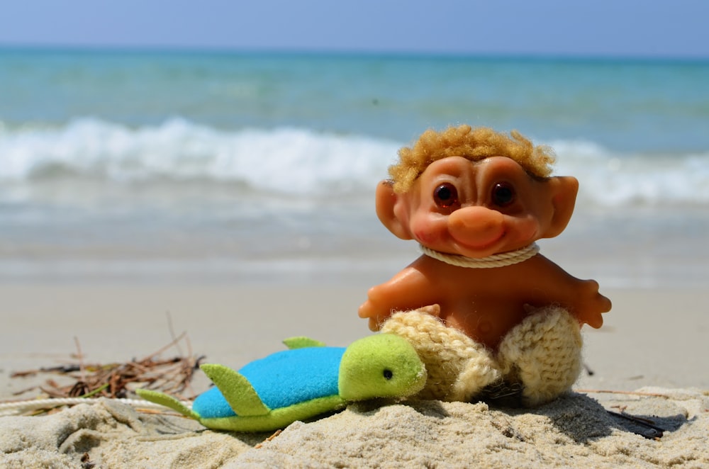 a toy monkey sitting on top of a beach next to a turtle