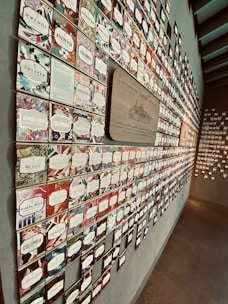 A wall display of numerous labels arranged in a grid, each with unique designs and colorful patterns. The labels include names of different countries, suggesting a theme related to coffee or global selection. The signage is mounted on a textured wall, with one prominent wooden plaque that reads 'Seattle' in the center.