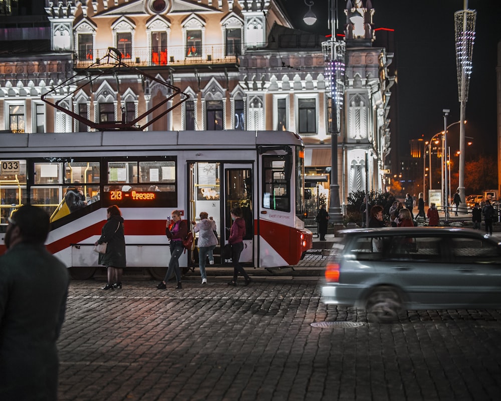 a group of people standing outside of a red and white bus