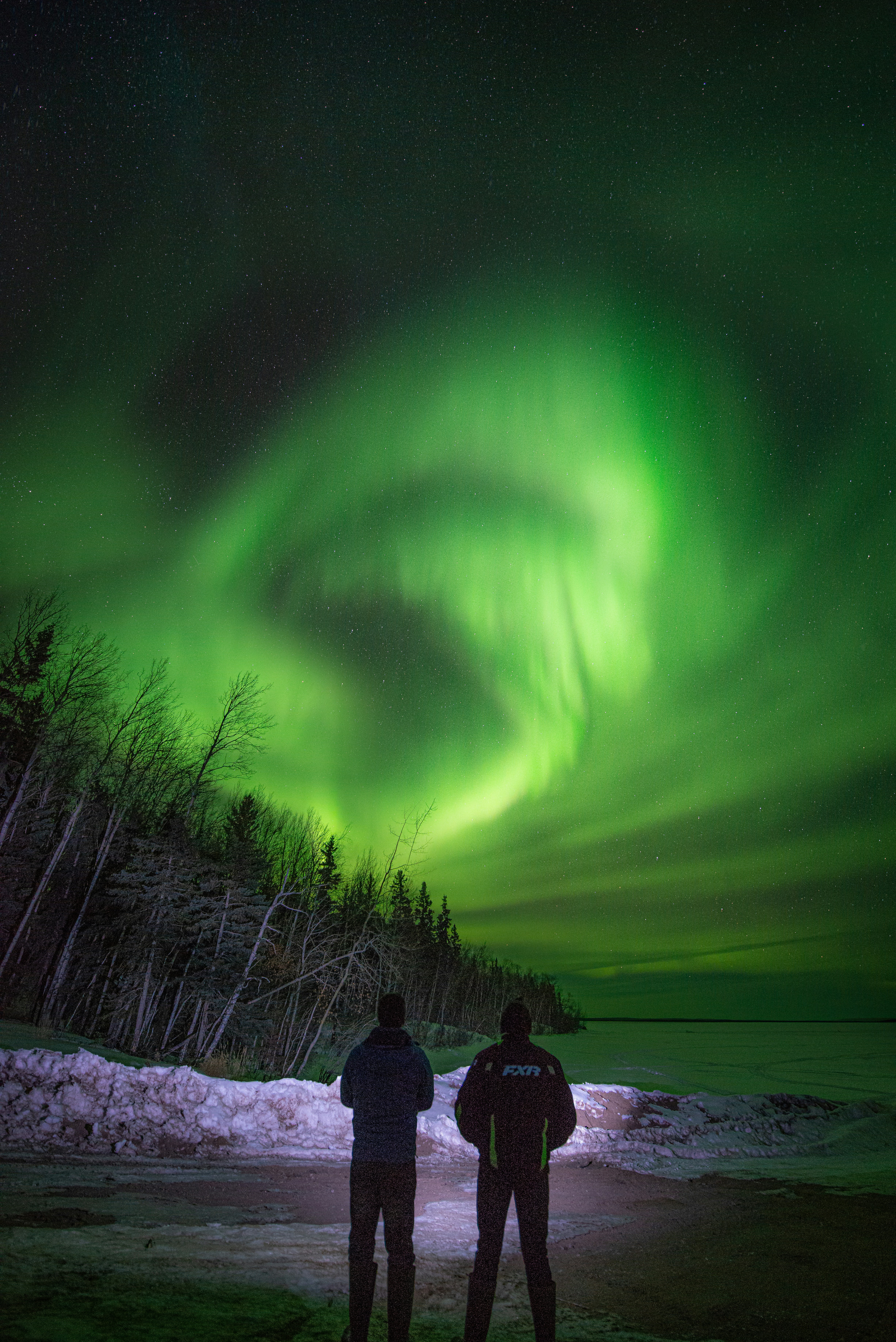 two people standing in front of a green aurora bore