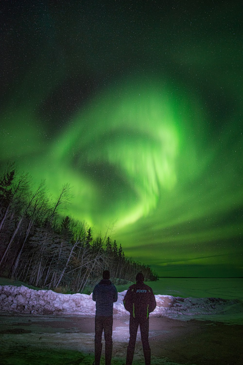 two people standing in front of a green aurora bore