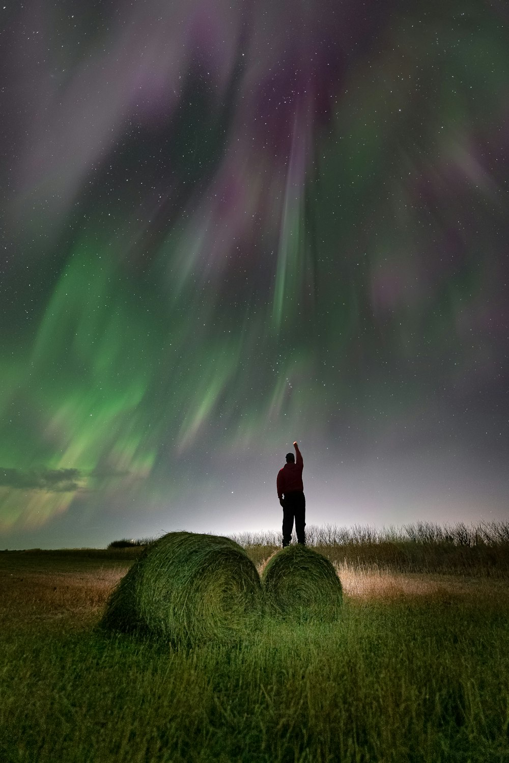 a man standing on a bale of hay under the aurora bore